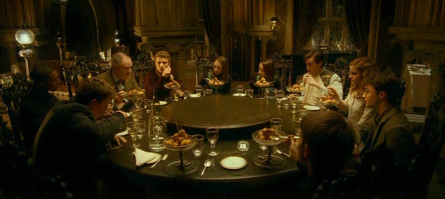 A screenshot of a scene from the 'Harry Potter and the Half-Blood Prince' film: Professor Slughorn sits at a round dining table with a small group of students. Placed in front of each person is a large raised dishes of profiteroles.