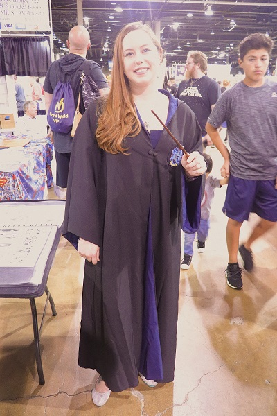 This Ravenclaw cosplayer is dressed in a Hogwarts robe and is holding a wand.