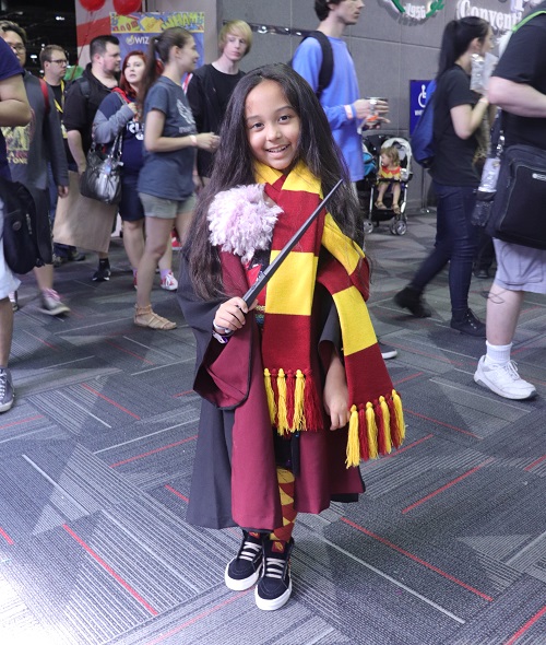 A child stands in front of a crowd wearing and red and yellow Gryffindor scarf and Hogwarts robes.
