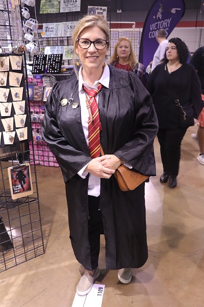 This cosplayer dressed in Gryffindor robes poses in front of a vendor.