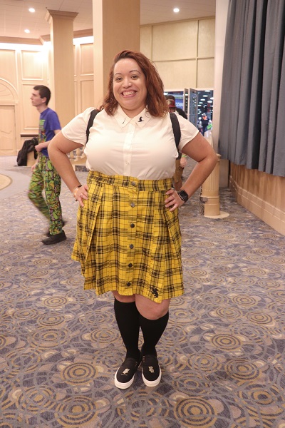 Smiling brightly, this cosplayer wears a black and yellow patterned skirt and knee high black socks.