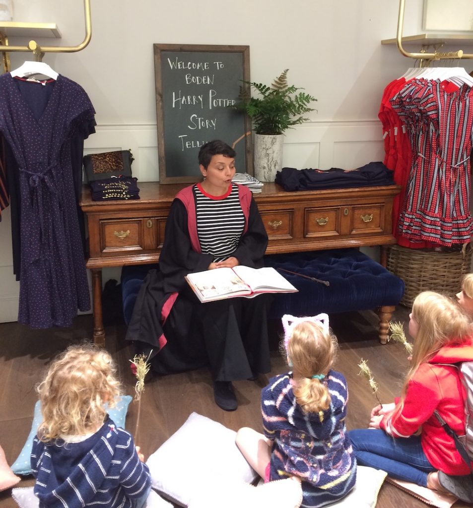 A women dressed in Harry Potter robes reads a chapter of "Harry Potter and the Philosopher's Stone" to a group of children who are sitting on the floor.