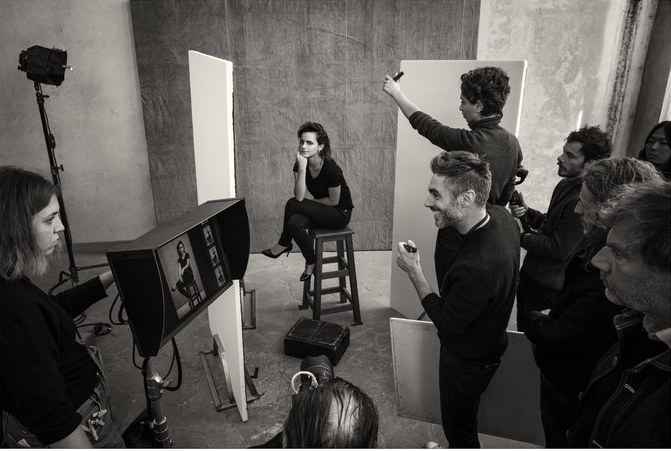 Emma Watson sits on a stool and is surrounded by lights and people during the Pirelli Calendar 2020 photoshoot.