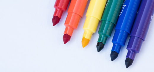 The tips of six markers (red, orange, yellow, green, blue, and purple) without lids are lined up in the upper-right corner on a white background.