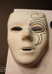 a white full-face mask with the beginnings of a black swirling pattern stenciled on