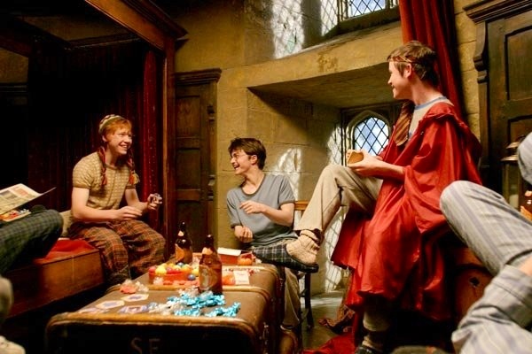 Ron, Harry, and Seamus relax in the gryffindor boys dorm, llaughing and eating candy. Dean and Neville are visible in the edge of the image.