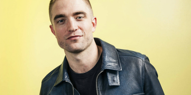 Robert Pattinson smiling in front of a yellow background