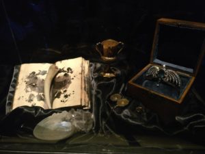 a display of movie props including Tom Riddle's ruined diary with the Basilisk fang, Slytherin's locket, Ravenclaw's diadem, Hufflepuff's cup, and the Gaunt family ring.\