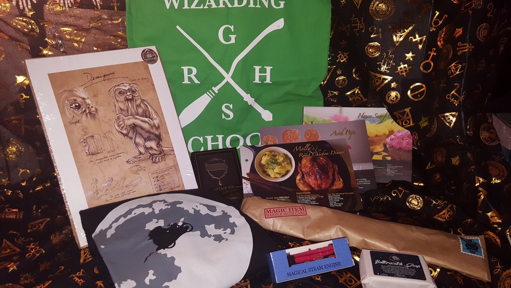 Geek Gear July 2018: Demiguise print, Slytherin tote bag, Slytherin Quidditch Captain’s pin, Hagrid silhouette T-shirt, magical steam engine miniature, butterscotch soap, wizarding world recipe cards, and wand wrapped in parchment paper