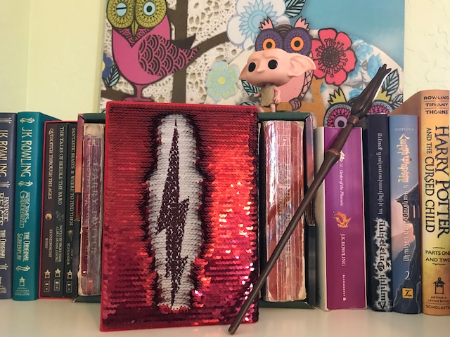 Harry Potter: Manage Your Mischief Marauder’s Map Sequin Notebook with alternate back cover partially revealed, displayed alongside “Harry Potter” books