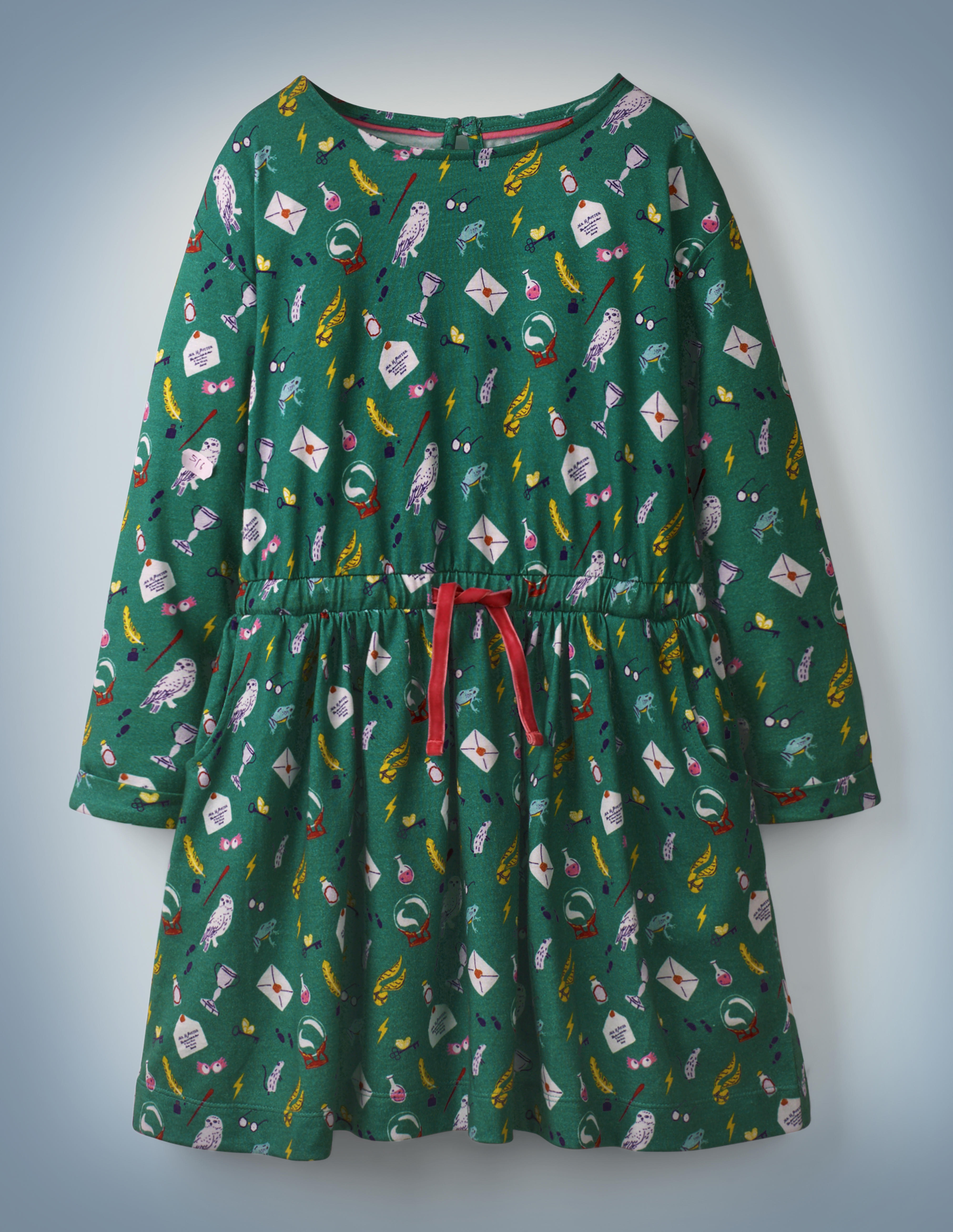 The Mini Boden Hogwarts Printed Dress in green features an all-over pattern of iconic “Harry Potter” images, including Luna Lovegood’s Spectrespecs, Hedwig, and a Hogwarts acceptance letter. The dress features a red drawstring in its center. It retails at £24.