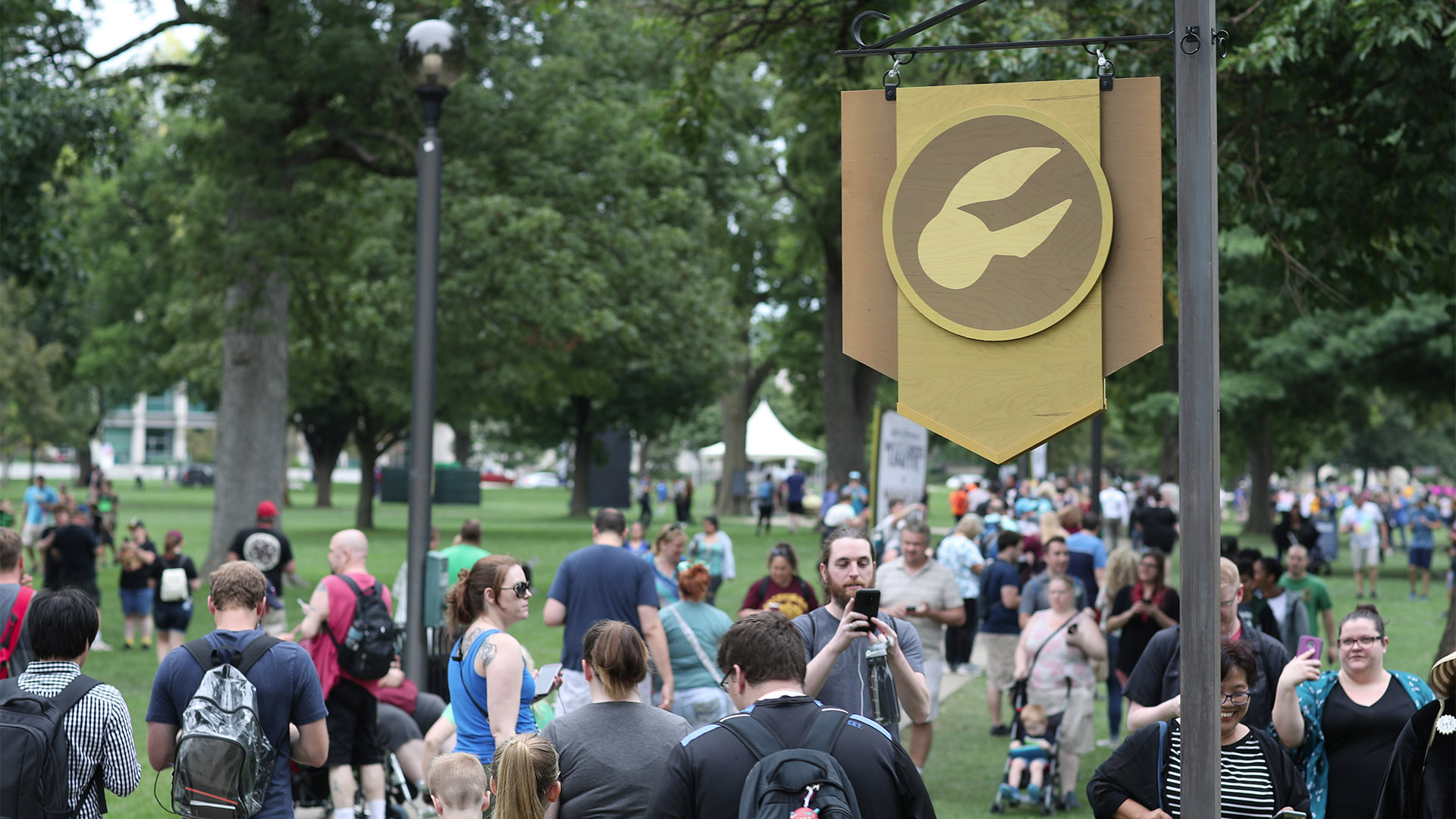 Players at the “Harry Potter: Wizards Unite” Fan Festival look for Department of Magical Games and Sports Foundables near a landmark flag.