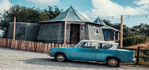 A blue car is parked in front of a Hagrid's Hut replica.
