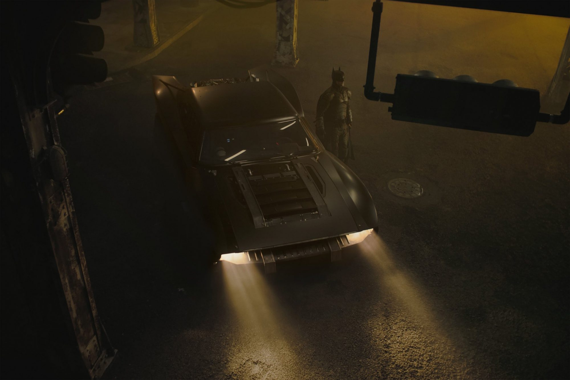 Robert Pattinson as Batman is pictured standing alongside the Batmobile.