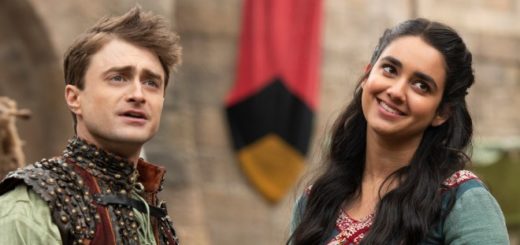 Daniel Radcliffe and Geraldine Viswanathan in Miracle Workers. They are dressed in colorful medieval clothes, Dan is looking a bit confused but Geraldine is smiling.