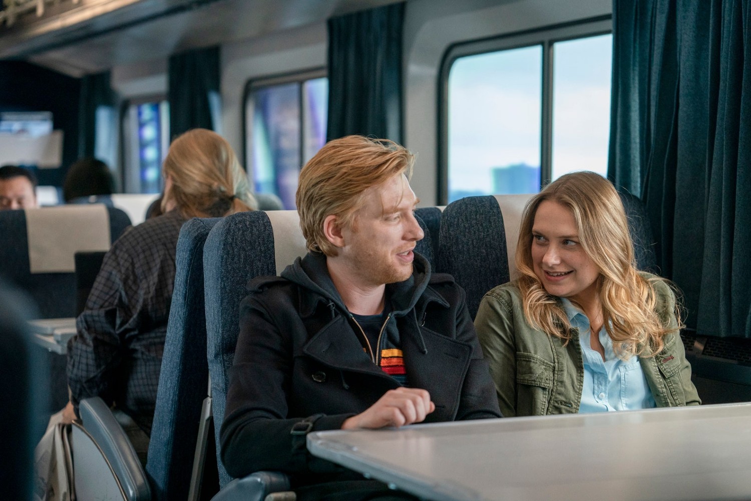 Domnhall Gleeson as Billy and Merritt Wever as Ruby sitting on a train in HBO series Run.