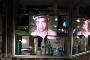 Robert Pattinson's face is projected on some toiler paper rolls on a bathroom shelf.
