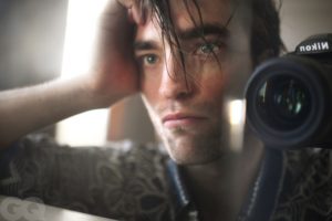Robert Pattinson taking a selfie through the mirror up close with a camera. He looks handsome and contemplative.