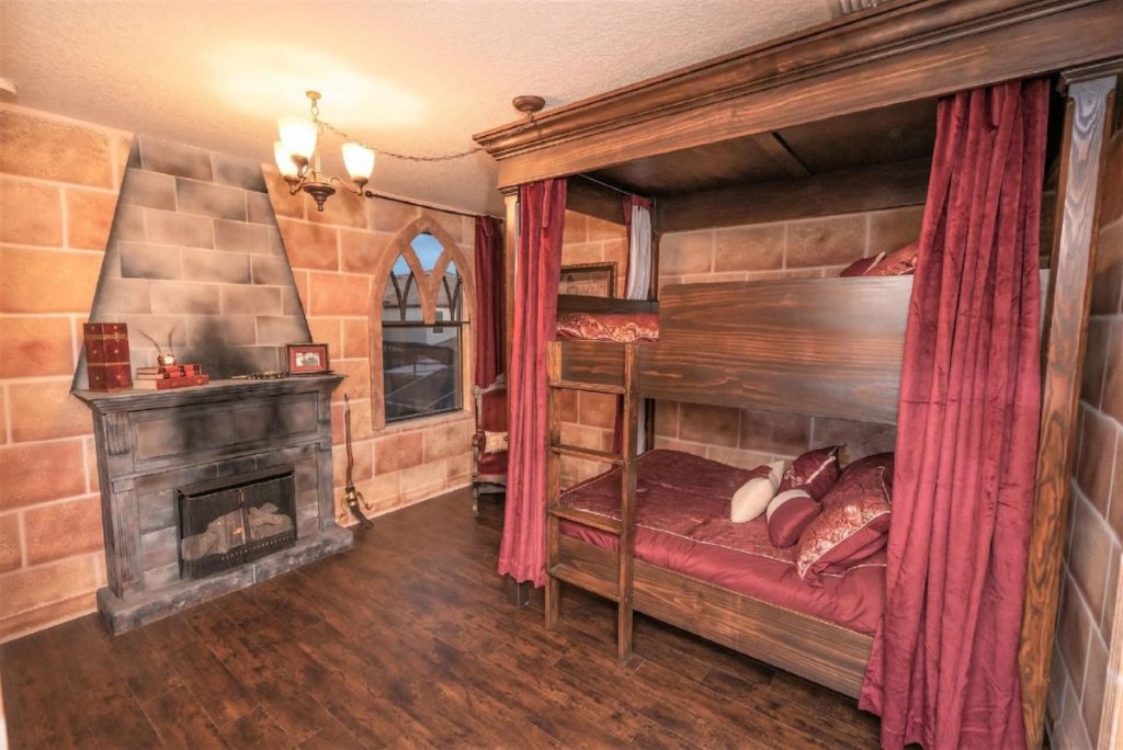 A set of two bunk beds is pictured in a Gryffindor-themed bedroom. There are crimson curtains ont he bed and a fireplace.