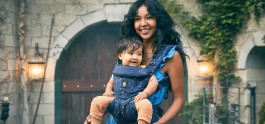 An adult and infant model the Omni 360 baby carrier from the Ergobaby Lumos Maxima Collection.