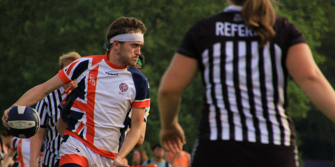 A chaser from the United Kingdom is holding a quaffle. There is a referee on the right and another referee in the background.