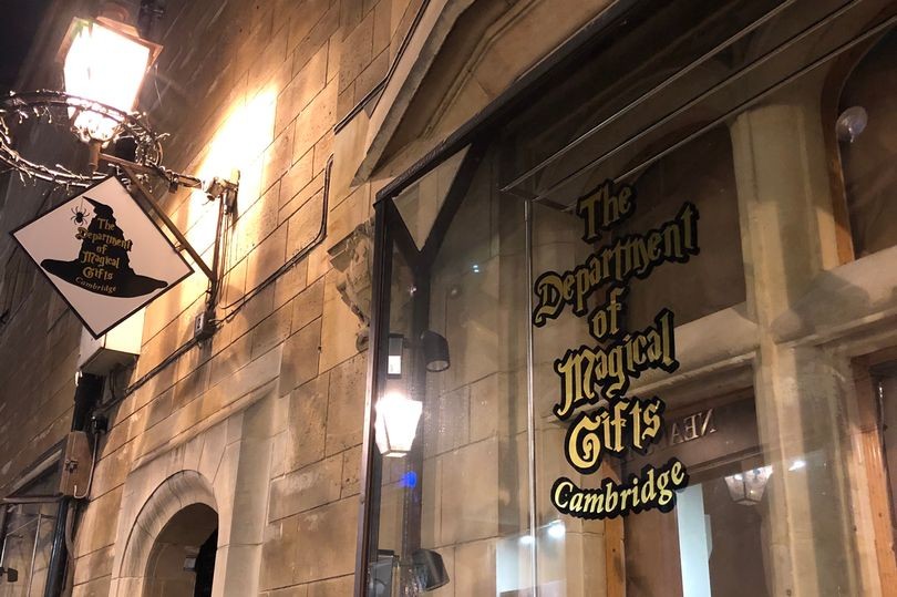 A historical shop facade in a stone building has an antique candelabra, and the label The Department of Magical Gifts on the window.
