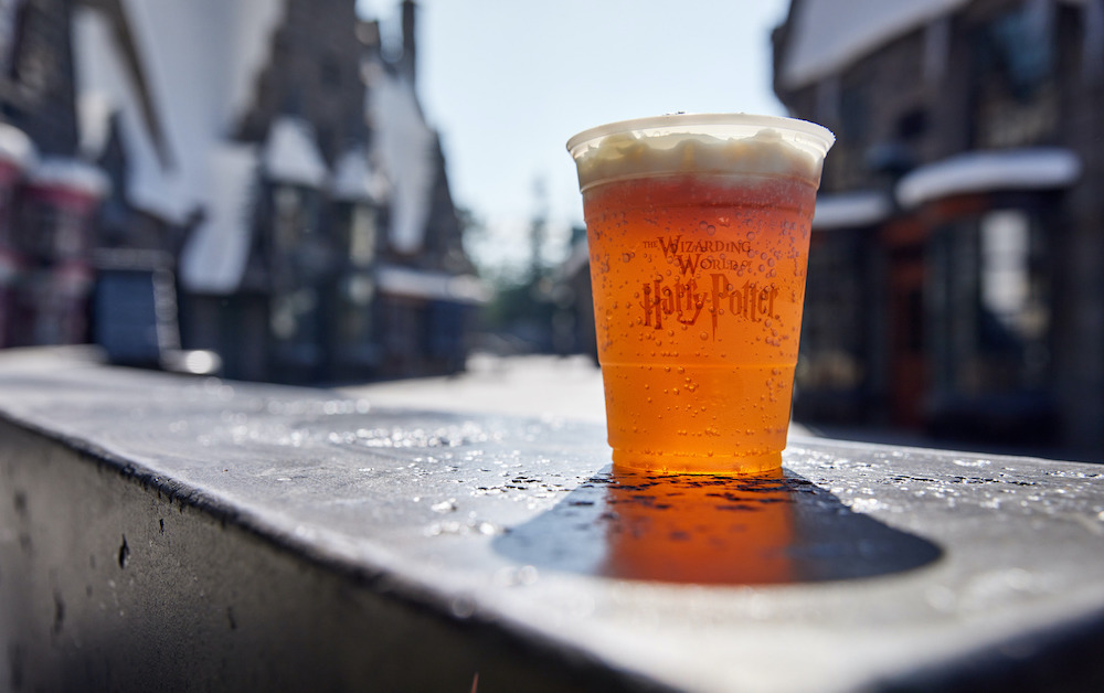 A plastic cup of butterbeer sits on a wall in the sunshine in Hogsmeade at The Wizarding World of Harry Potter at Universal Studios Hollywood.