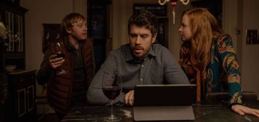 In a still from Season 2 of "Servant", Rupert Grint (who plays Julian Pearce) waves a wine glass in mid-discussion with Toby Kebbel (who plays Sean Turner) and Lauren Ambrose (who plays Dorothy Turner).