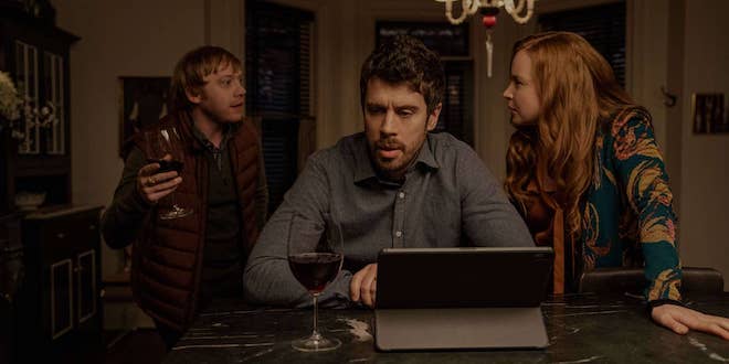 In a still from Season 2 of "Servant", Rupert Grint (who plays Julian Pearce) waves a wine glass in mid-discussion with Toby Kebbel (who plays Sean Turner) and Lauren Ambrose (who plays Dorothy Turner).