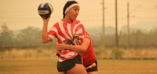 There is a female chaser in red and white jersey holding a quaffle. Another chaser or keeper in a red jersey is trying to tackle her.