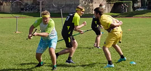 Bradley Walsh is shown in a Slovenian jersey, holding his broom in his hands (being “off broom”). Barney Walsh is pictured beside him in an Aemona Argonauts jersey, standing in front of the snitch runner. Another Aemona Argonauts player and three hoops are visible in the background.