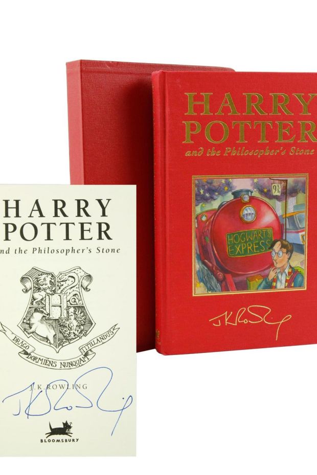 A bright red deluxe copy of Harry Potter and the Philosopher's Stone is pictured on a white backdrop, plus the title page signed by J. K. Rowling.