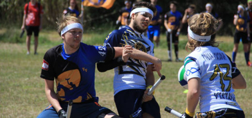 A chaser in a Vienna Vanguards jersey attempts to grab a chaser from the opposing team, while another chaser holding a quaffle looks on.