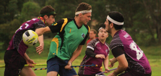 There is one chaser in a green jersey holding a quaffle, and two chasers and one keeper in violet jerseys are trying to stop them.