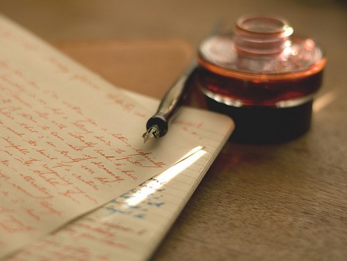 quill and ink bottle laying on top of parchment paper