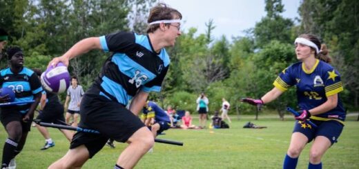 A chaser from the Ottawa Black Bears runs forward from the left while holding a quaffle. A chaser from the Washington Admirals is shown at the right, while a beater from the Ottawa Black Bears is shown in the background at the left.