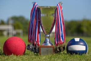 The Benepe Cup, the trophy for MLQ Championship, is shown with medals hanging off of it. The trophy itself is silver and sits on a wooden base with a plaque.