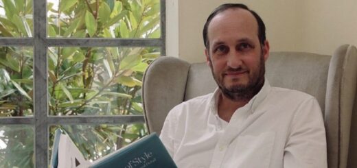 Gary Tomkins is posing for a portrait in an armchair with a book by a window.