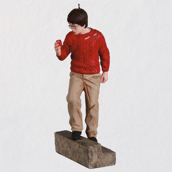 Against a white backdrop, a lifelike ornament of 11-year old Harry is pictured as he is holding the Sorcerer's Stone, in the red sweater and brown pants as seen in the movie.