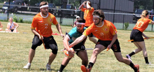 Eight quidditch players in orange jerseys are pictured, and one of the chasers is trying to take the quaffle from another chaser in a cyan jersey.