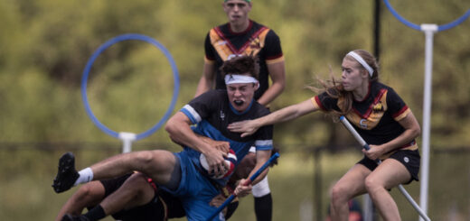 There is a chaser from New York Titans who is trying to block or take the ball from the chaser of Austion Outlaws. Keeper from New York is standing behind them.