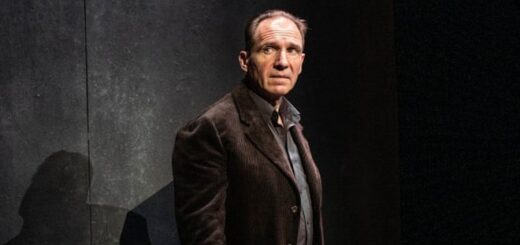 Ralph Fiennes is posing against a dark set in performance of Four Quartets on stage.