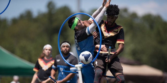There is a chaser from New York Titans who threw a quaffle through the hoops. A keeper from Austin Outlaws is trying to stop him. Chaser from New York Titans and chaser from Austin Outlaws are watching them in the background.