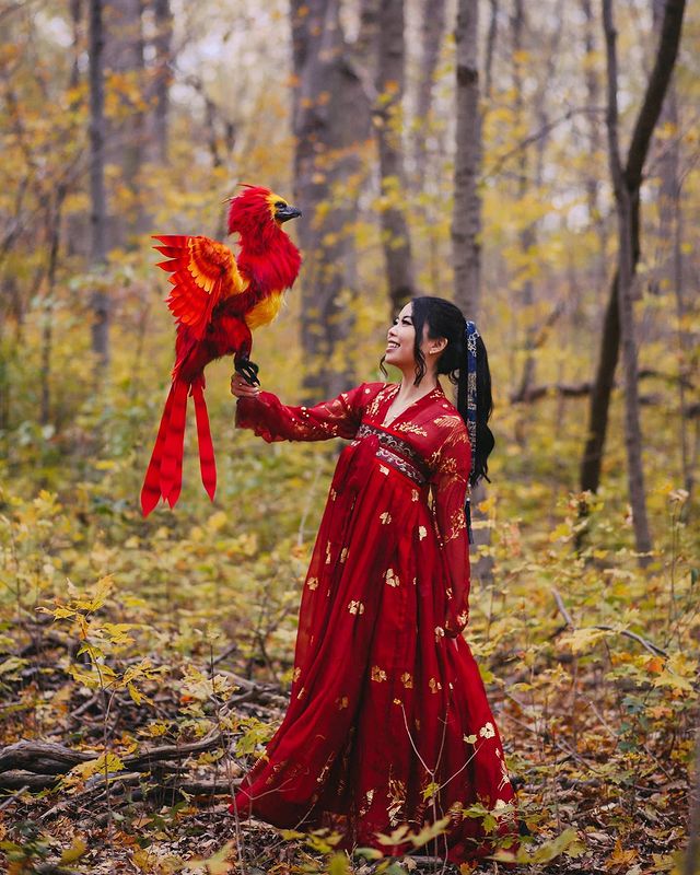 A woman stands in a forest with a mythical Phoenix on her arm