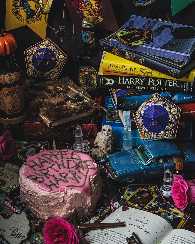 A pink cake like the one Hagrid gave Harry Potter sits on a beautifully styled table, full of Harry Potter objects