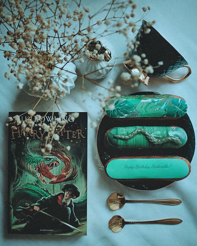 A Slytherin-themed still life includes flowers and a green copy of a Harry Potter book