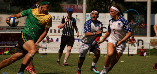 There is a keeper from the Australian team that is holding a quaffle and running forward. There are two chasers from the US team that are running to him. One referee is in the background.