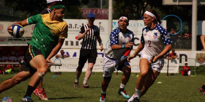 There is a keeper from the Australian team that is holding a quaffle and running forward. There are two chasers from the US team that is running to him. One referee is in the background.