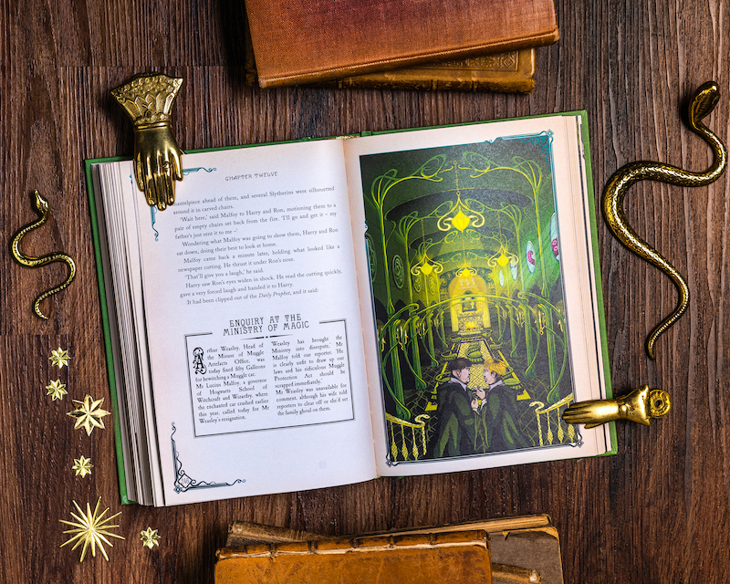 A copy of MinaLima' "Harry Potter and the Chamber of Secrets" is opened on a page showing the Slytherin Common Room.