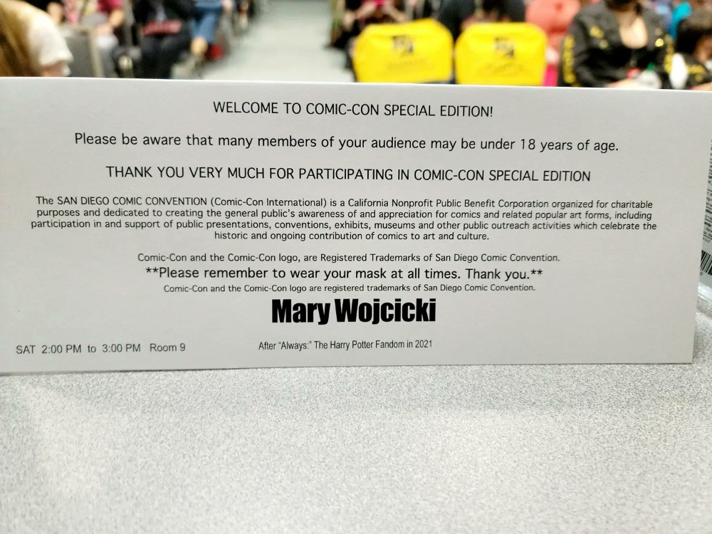The view from the back of a San Diego Comic-Con Special Edition name placard is shown. The audience is partially visible beyond it.
